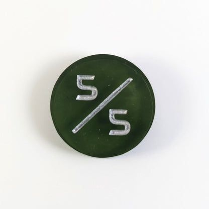 A top down photo of a dark green 5/5 token with silver numbers sits on a white background.