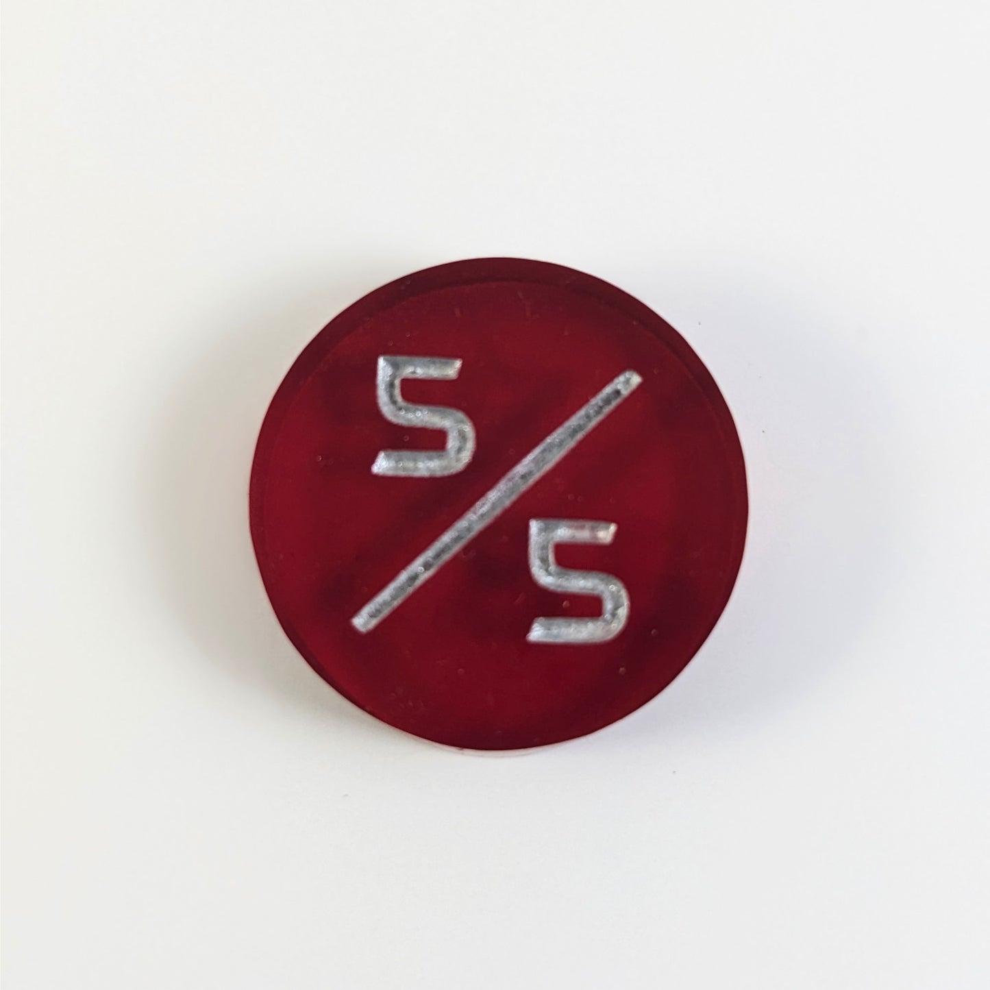 A top down photo of a red 5/5 token with silver numbers sits on a white background.