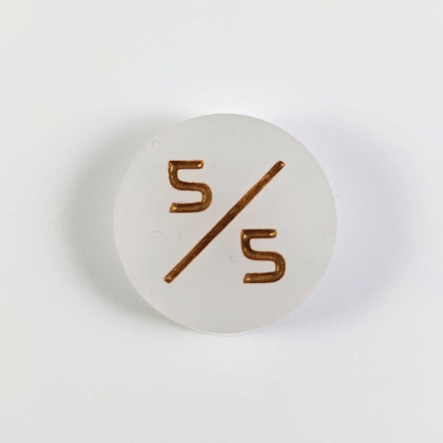 A top down photo of a white 5/5 token with gold numbers sits on a white background.