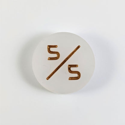 A top down photo of a white 5/5 token with gold numbers sits on a white background.