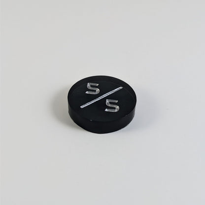 A low angle photo of a black 5/5 token with silver numbers sits on a white background.