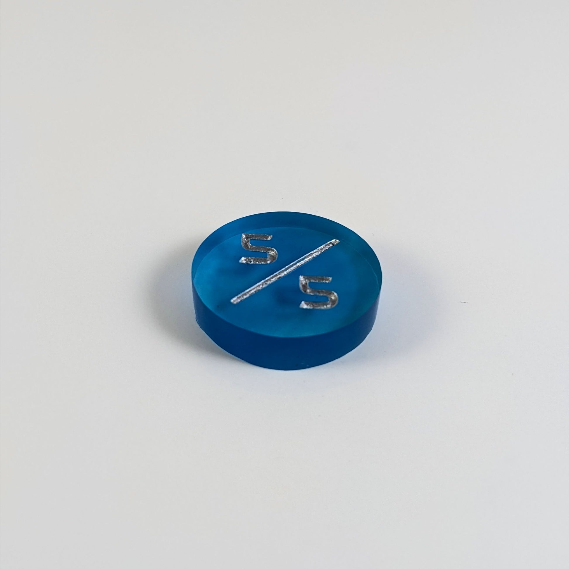 A low angle photo of a blue 5/5 token with silver numbers sits on a white background.