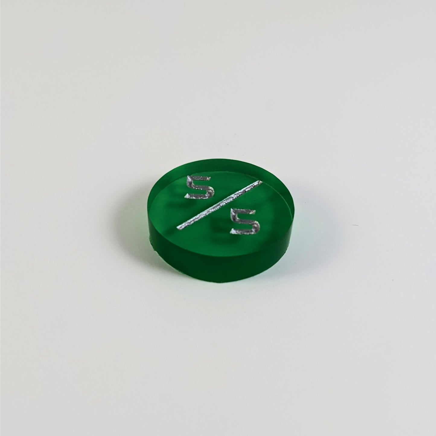 A low angle photo of a green 5/5 token with silver numbers sits on a white background.