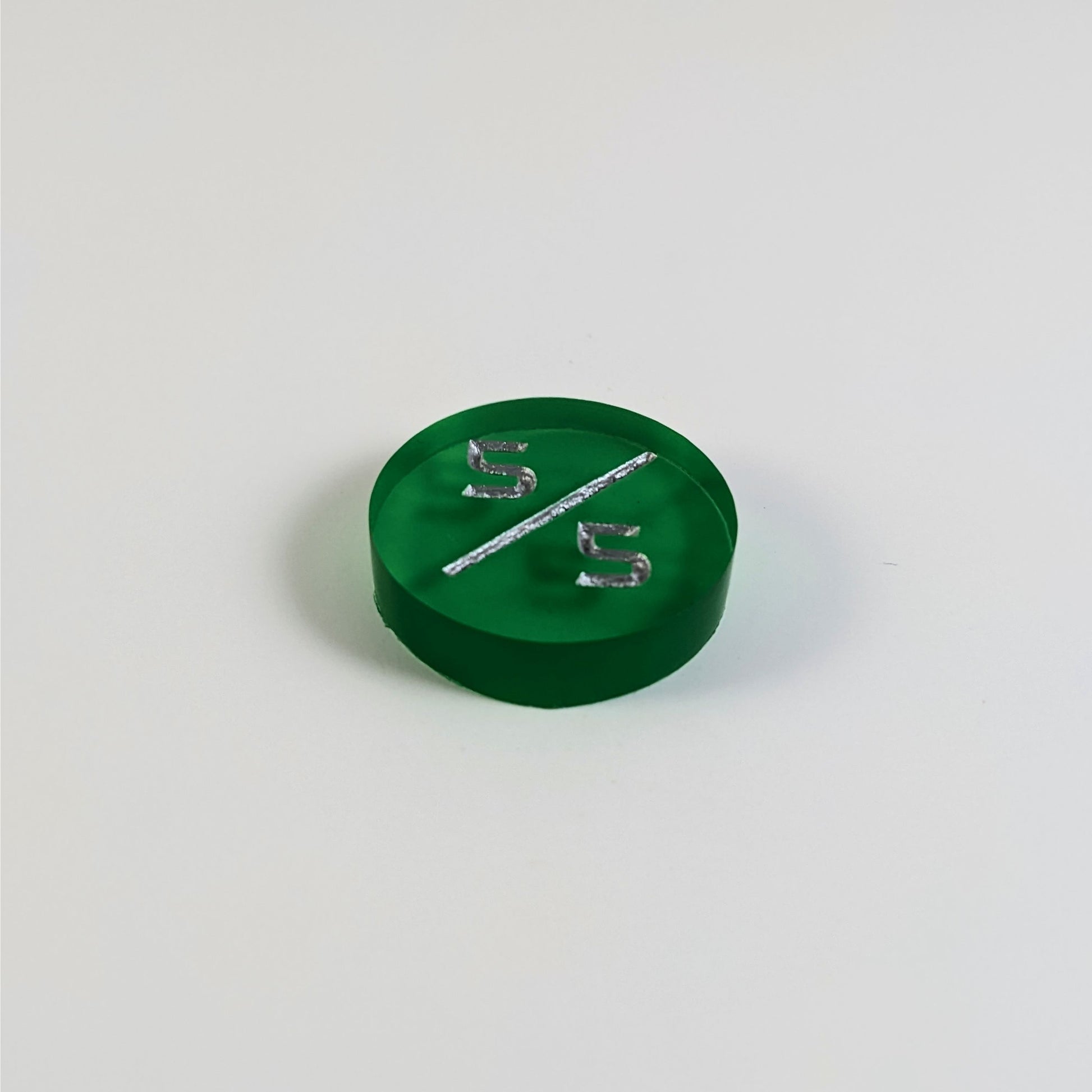 A low angle photo of a green 5/5 token with silver numbers sits on a white background.