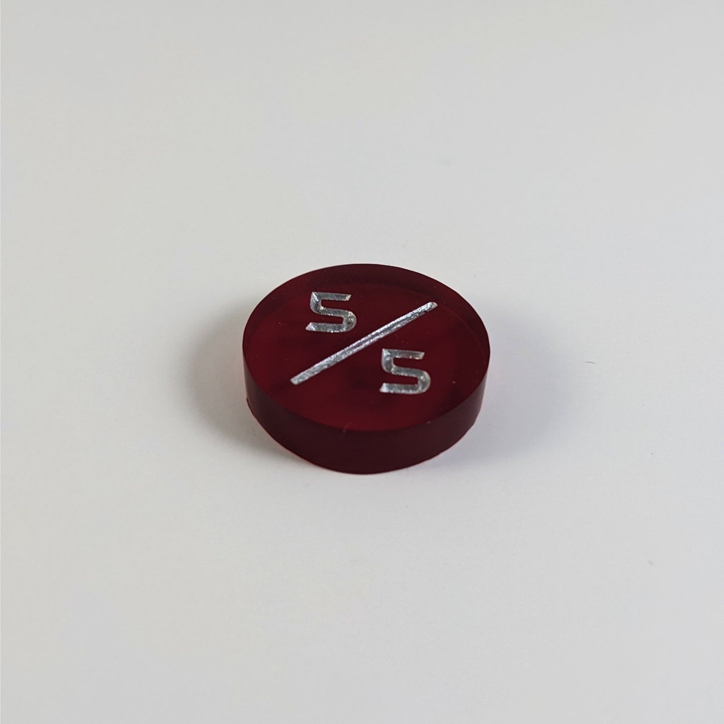 A low angle photo of a red 5/5 token with silver numbers sits on a white background.