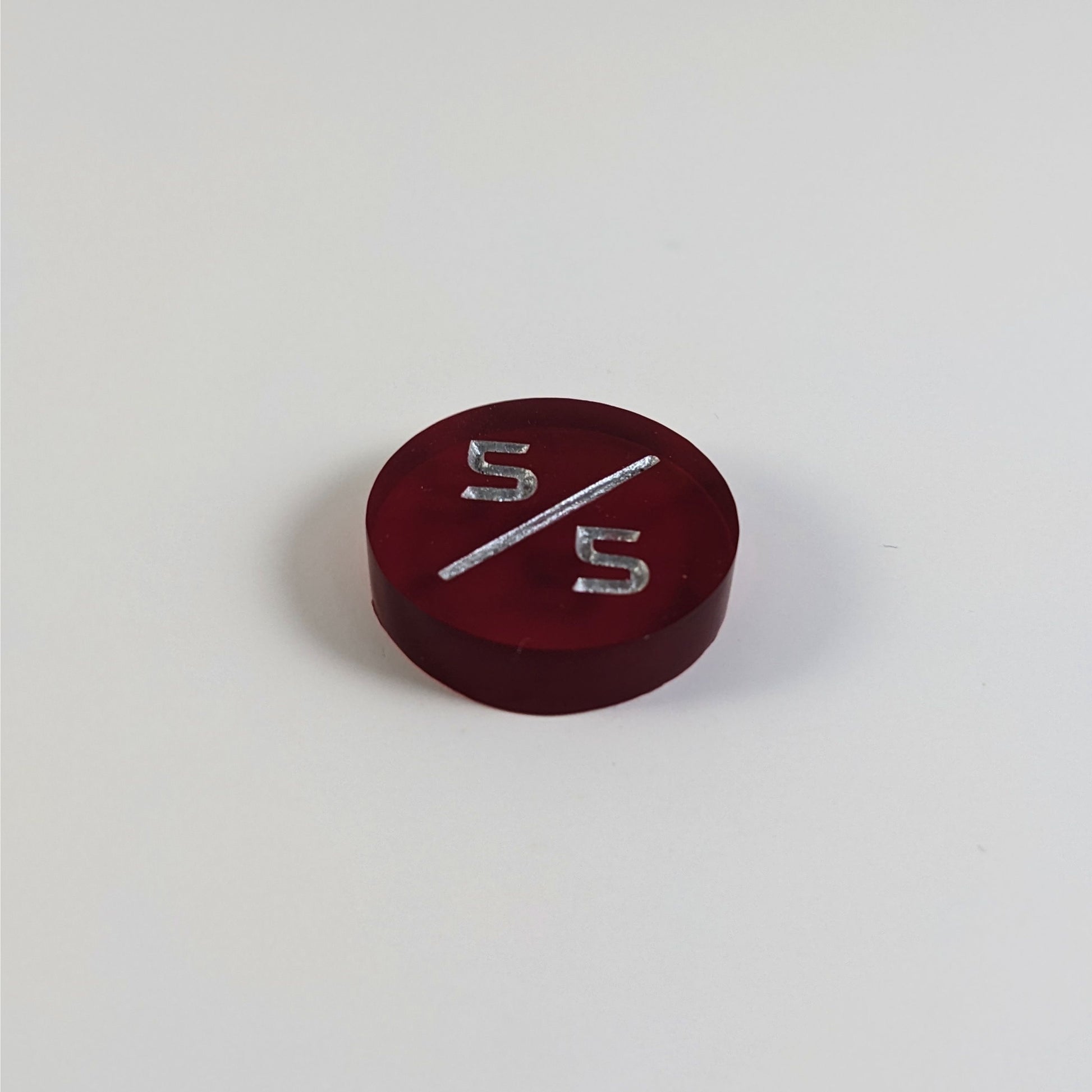 A low angle photo of a red 5/5 token with silver numbers sits on a white background.