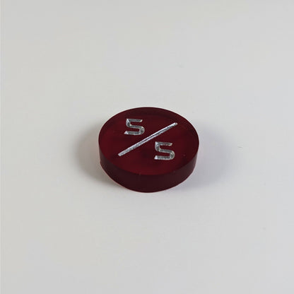 A low angle photo of a red 5/5 token with silver numbers sits on a white background.