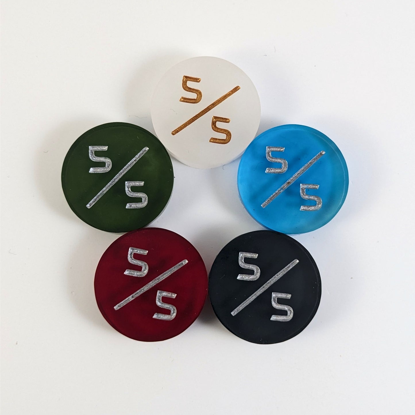 Five 5/5 tokens arranged in a circle face up. White with gold numbers is at the top and blue, black, red, and dark green all with silver numbers follow going clockwise.