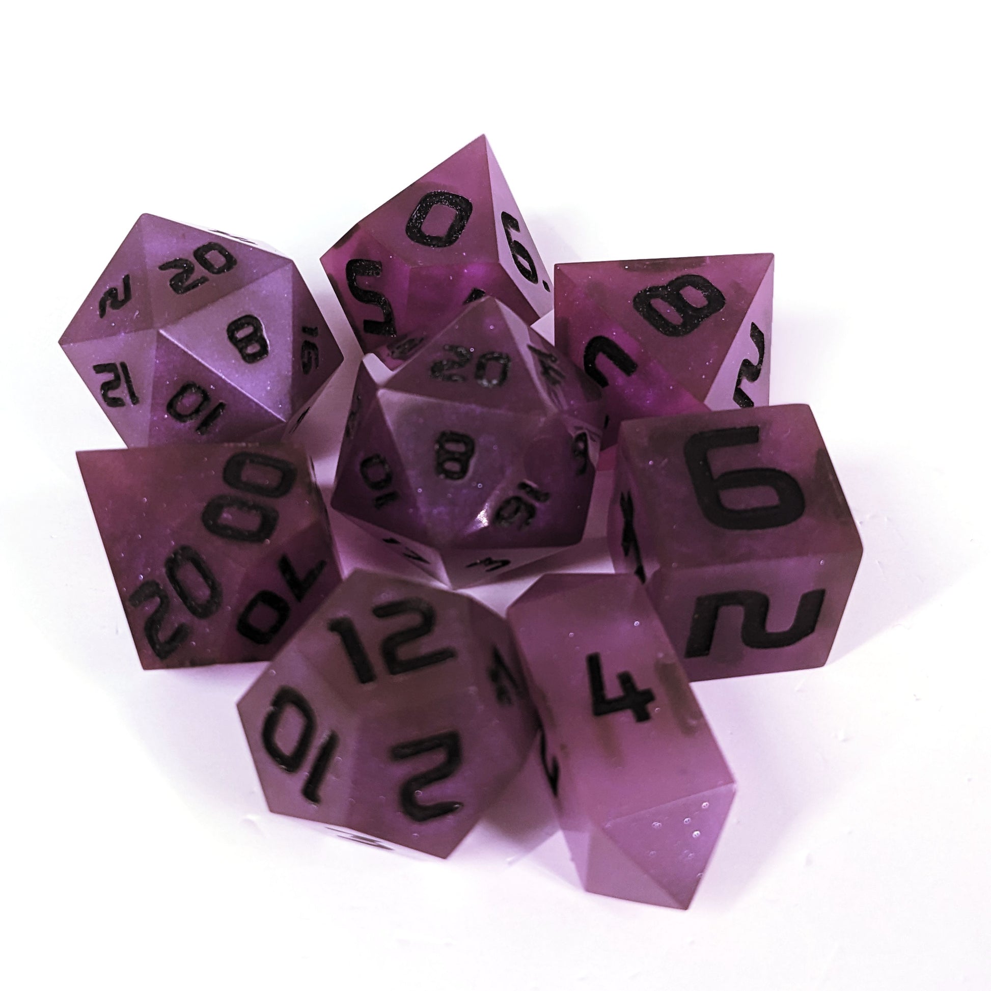 A complete set of 8 handmade artisan dice that are deep purple with black numbers. The DnD dice set is arranged in a circle and features 2 D20s, one of which is in the center surrounded by the other 7 dice on a white background. The d4 is a unique, crystalline shape.
