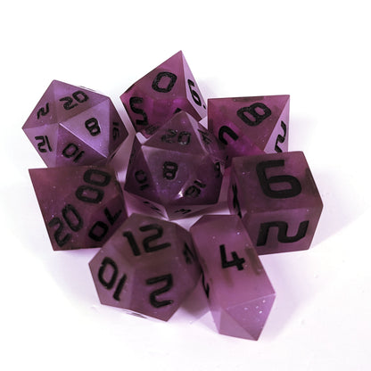A complete set of 8 handmade artisan dice that are deep purple with black numbers. The DnD dice set is arranged in a circle and features 2 D20s, one of which is in the center surrounded by the other 7 dice on a white background. The d4 is a unique, crystalline shape.