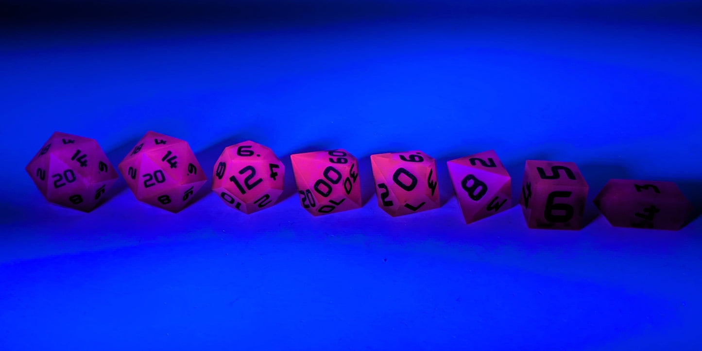 A straight on photo of a complete set of polyhedral dice that are deep purple with black numbers arranged in a straight line. They are lined up with the 2 d20s on the left going down to the d4 on the right side. The highest value number of each die is facing forward. The dice are under a UV light causing them to glow pink and the background is tinted blue.