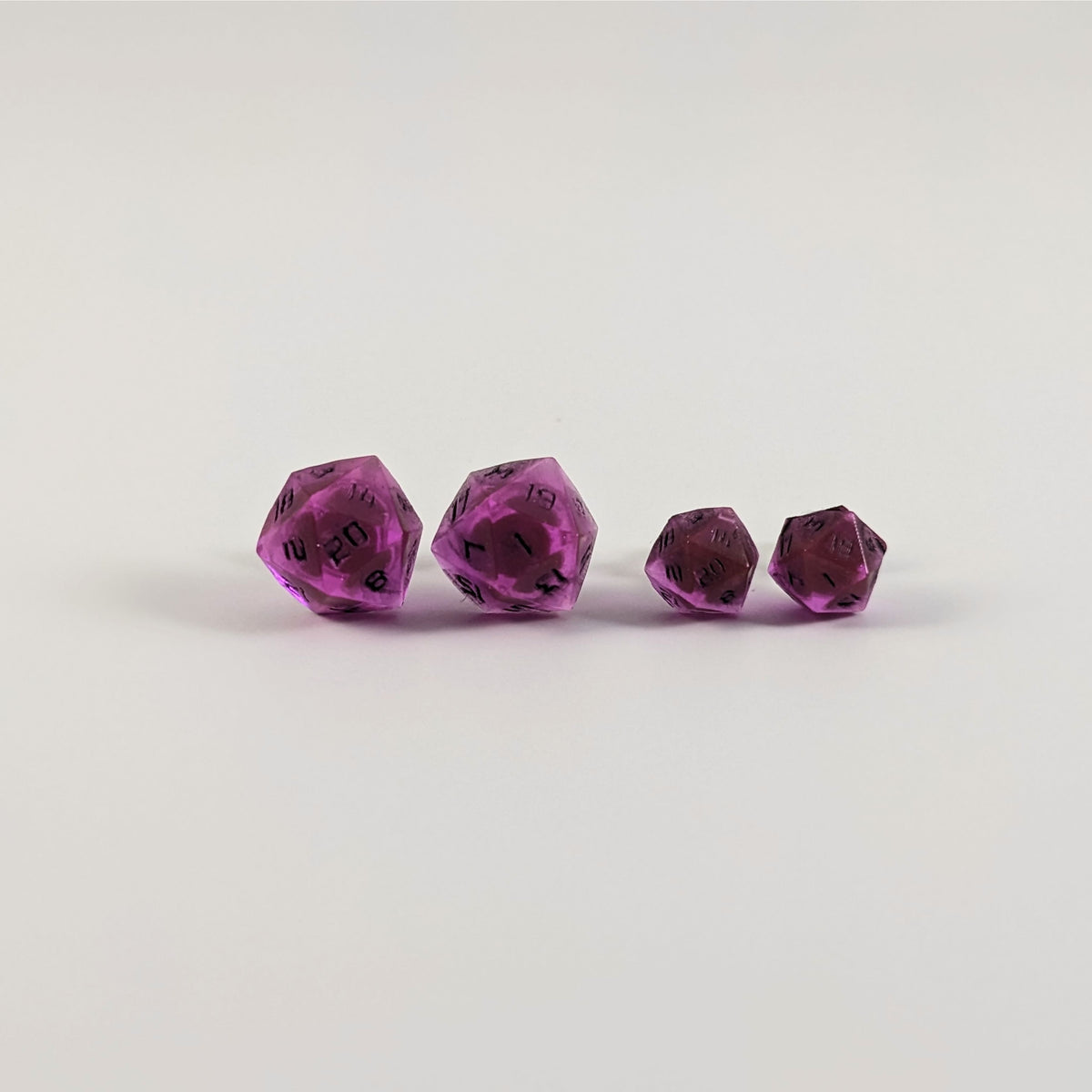 Two pairs of handmade d20 earrings with titanium hardware that are amethyst purple with black numbers on a white background sit in a line with the larger pair on the left and the smaller pair on the right. The earrings on the left of each pair centers the 20 face and the earrings on the right of each pair centers the 1 face.