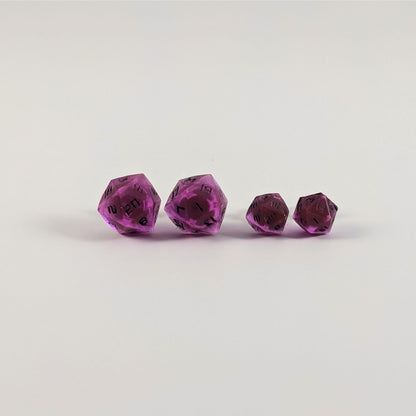Two pairs of handmade d20 earrings with titanium hardware that are amethyst purple with black numbers on a white background sit in a line with the larger pair on the left and the smaller pair on the right. The earrings on the left of each pair centers the 20 face and the earrings on the right of each pair centers the 1 face.