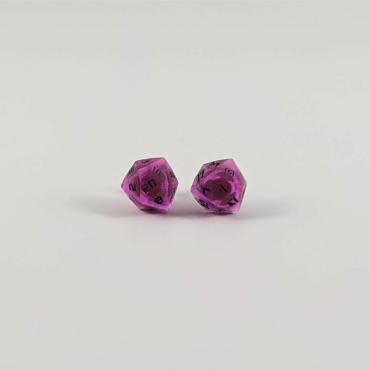 A single pair of the larger size handmade d20 earrings with titanium hardware that are amethyst purple with black numbers on a white background. The earring on the left centers the 20 face and the earring on the right centers the 1 face.