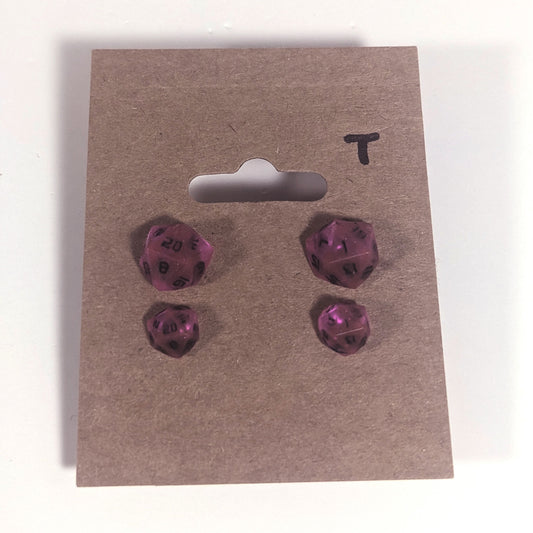 Two pairs of handmade d20 earrings with titanium hardware that are amethyst purple with black numbers on a kraft brown earring card with a T in the top right corner. The earrings on the left of each pair centers the 20 face and the earrings on the right of each pair centers the 1 face.