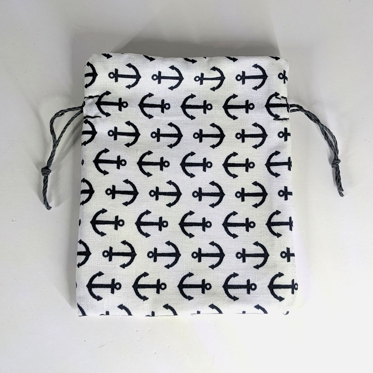 A small, handmade dice bag that is white with a navy anchor pattern lays flat on a white background.