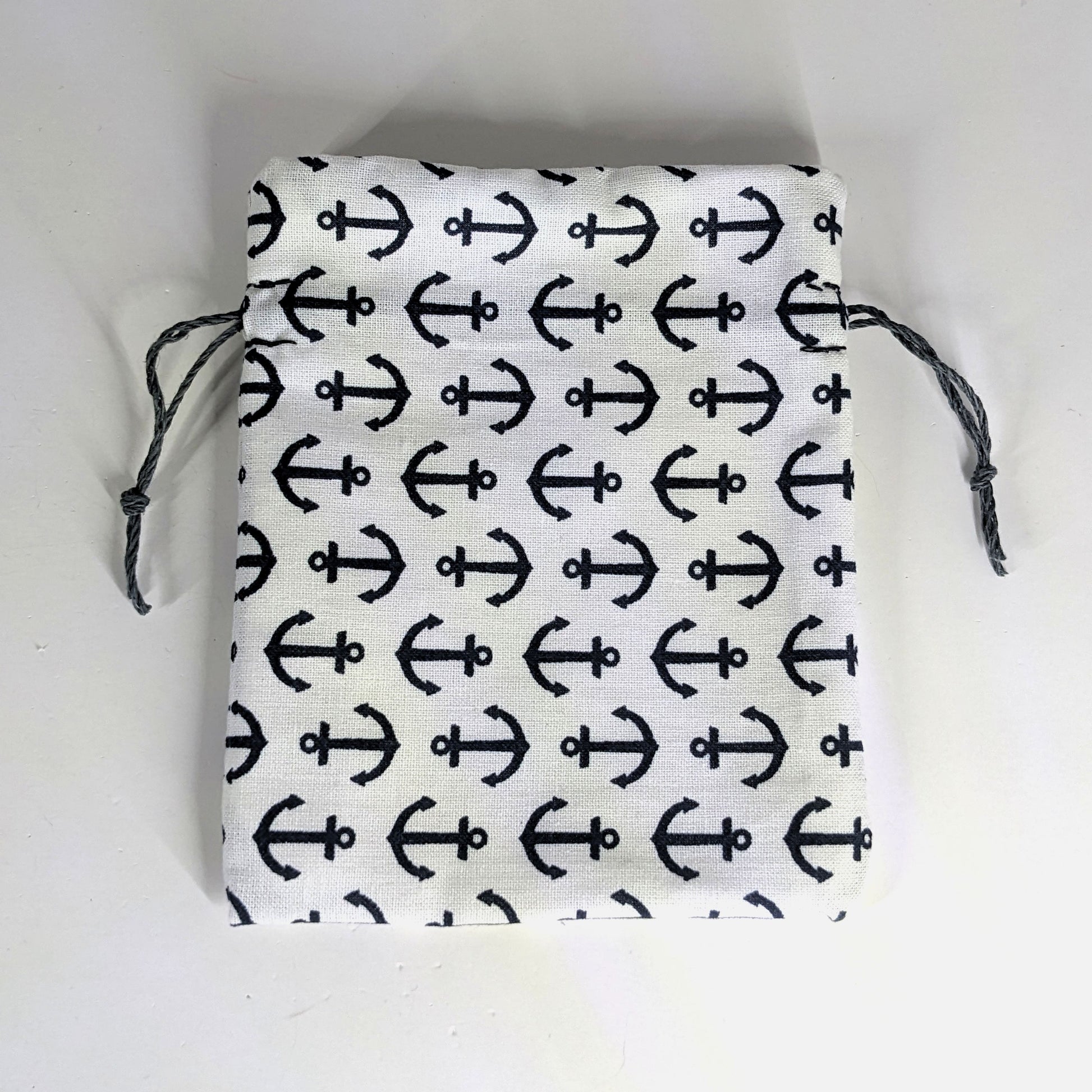 A small, handmade dice bag that is white with a navy anchor pattern lays flat on a white background.