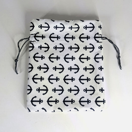 A small, handmade dice bag that is white with a navy anchor pattern lays flat on a white background.
