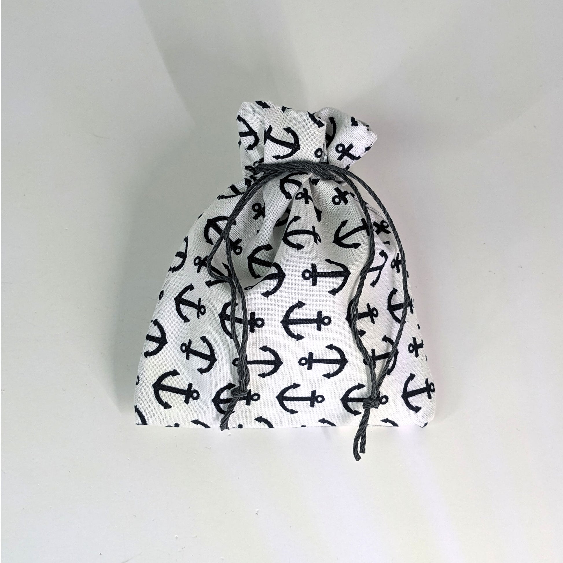 A small, handmade dice bag that is white with a navy anchor pattern is tied closed on a white background.