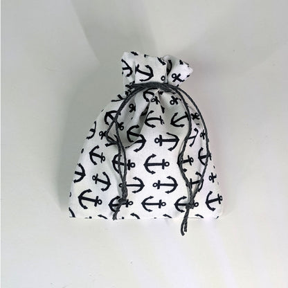 A small, handmade dice bag that is white with a navy anchor pattern is tied closed on a white background.