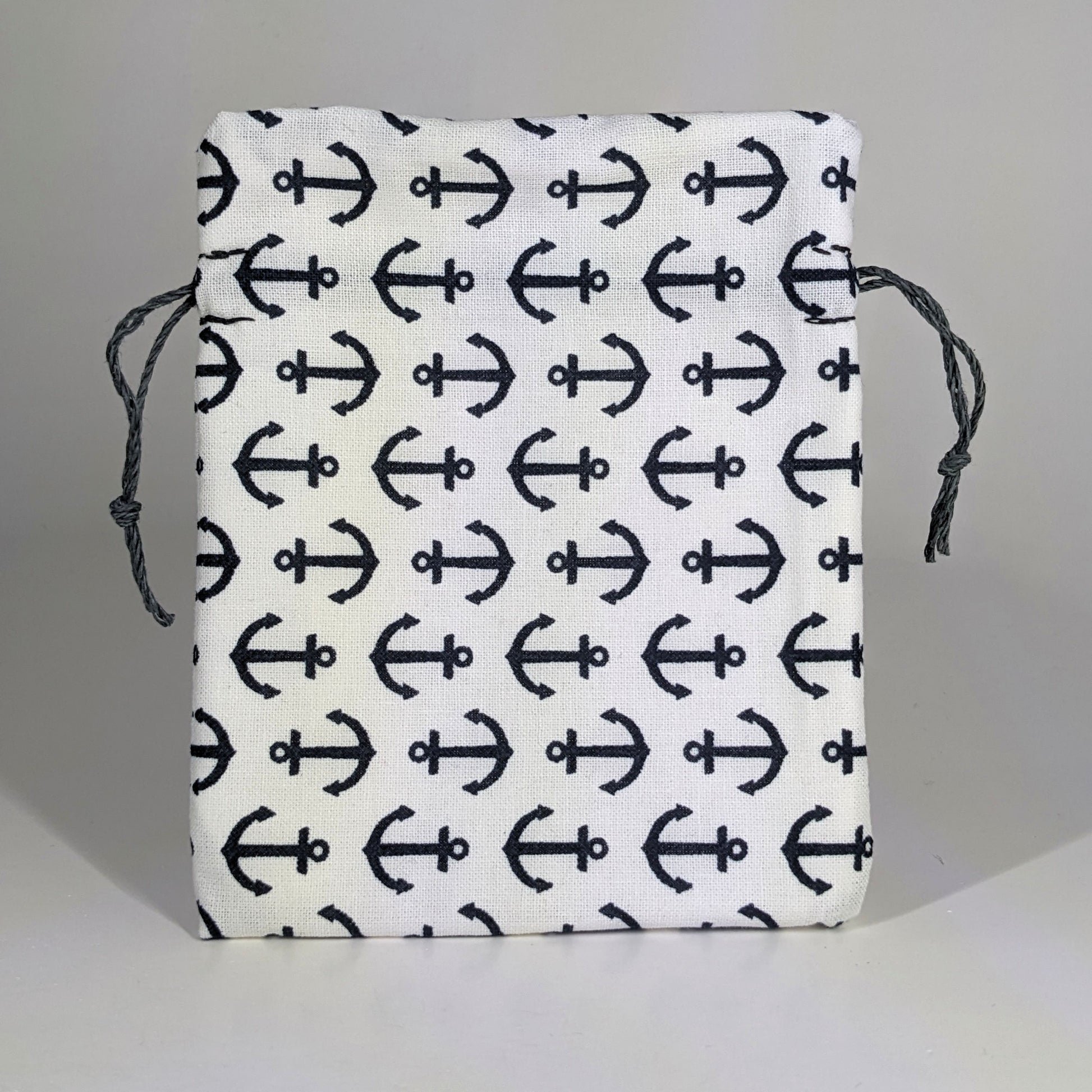 A small, handmade dice bag that is white with a navy anchor pattern stands upright on a white background.