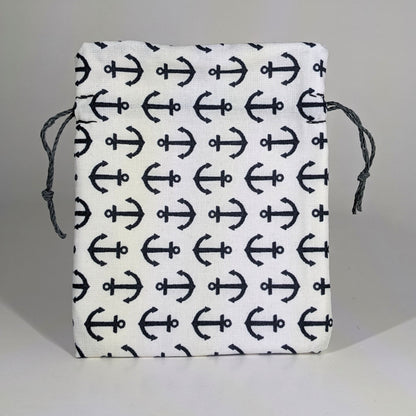 A small, handmade dice bag that is white with a navy anchor pattern stands upright on a white background.