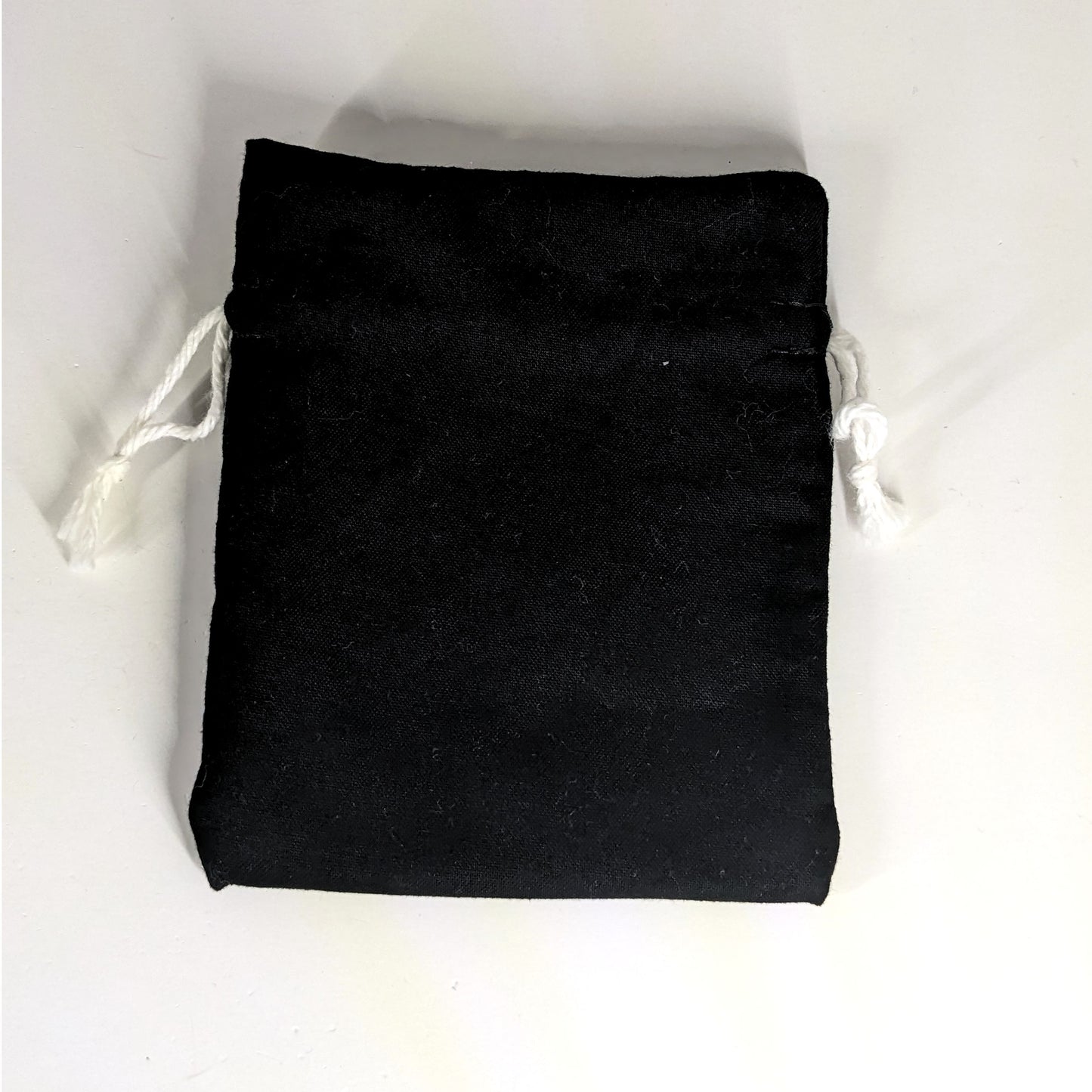 A small, handmade dice bag that is black lays flat on a white background.