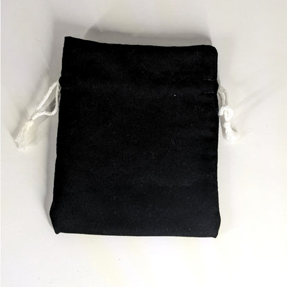 A small, handmade dice bag that is black lays flat on a white background.