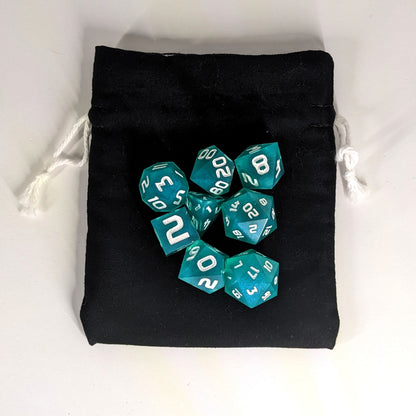 A small, handmade dice bag that is black lays flat on a white background with a set of teal dnd dice with white numbers sitting on top of it.