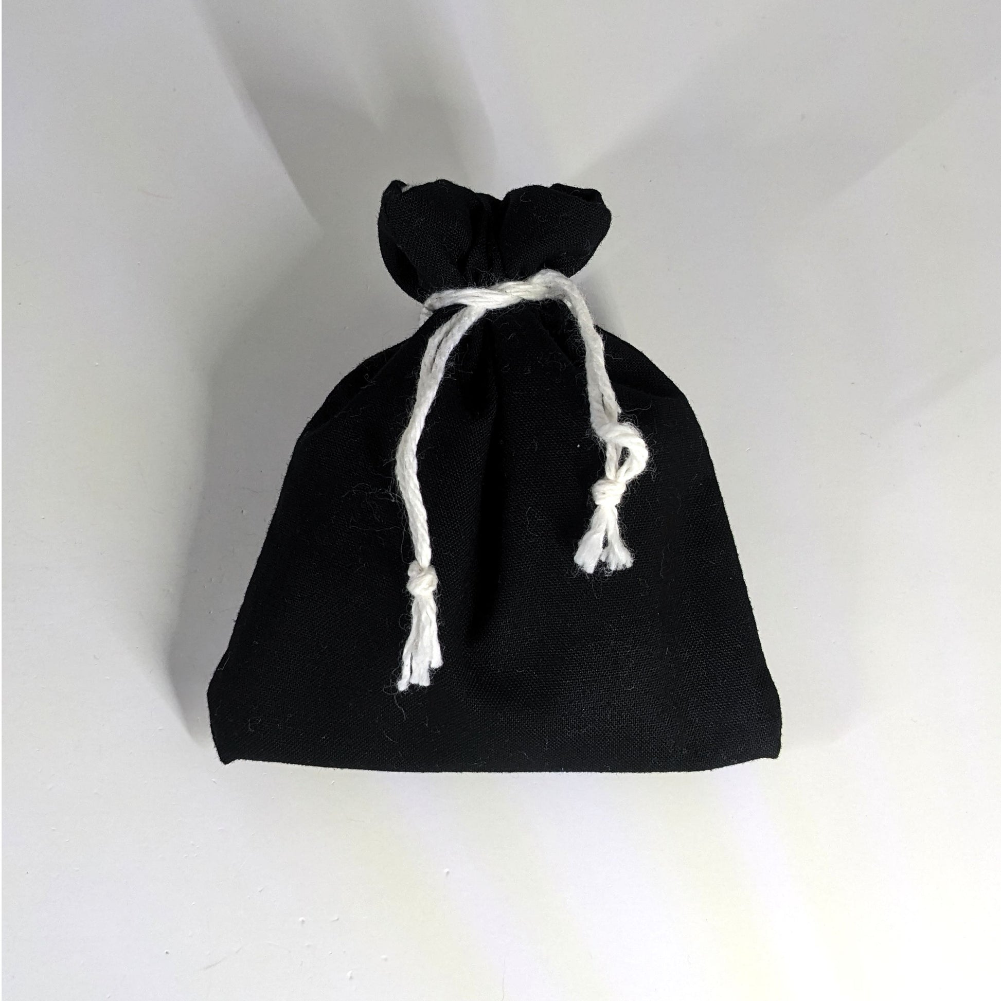 A small, handmade dice bag that is black is tied closed on a white background.