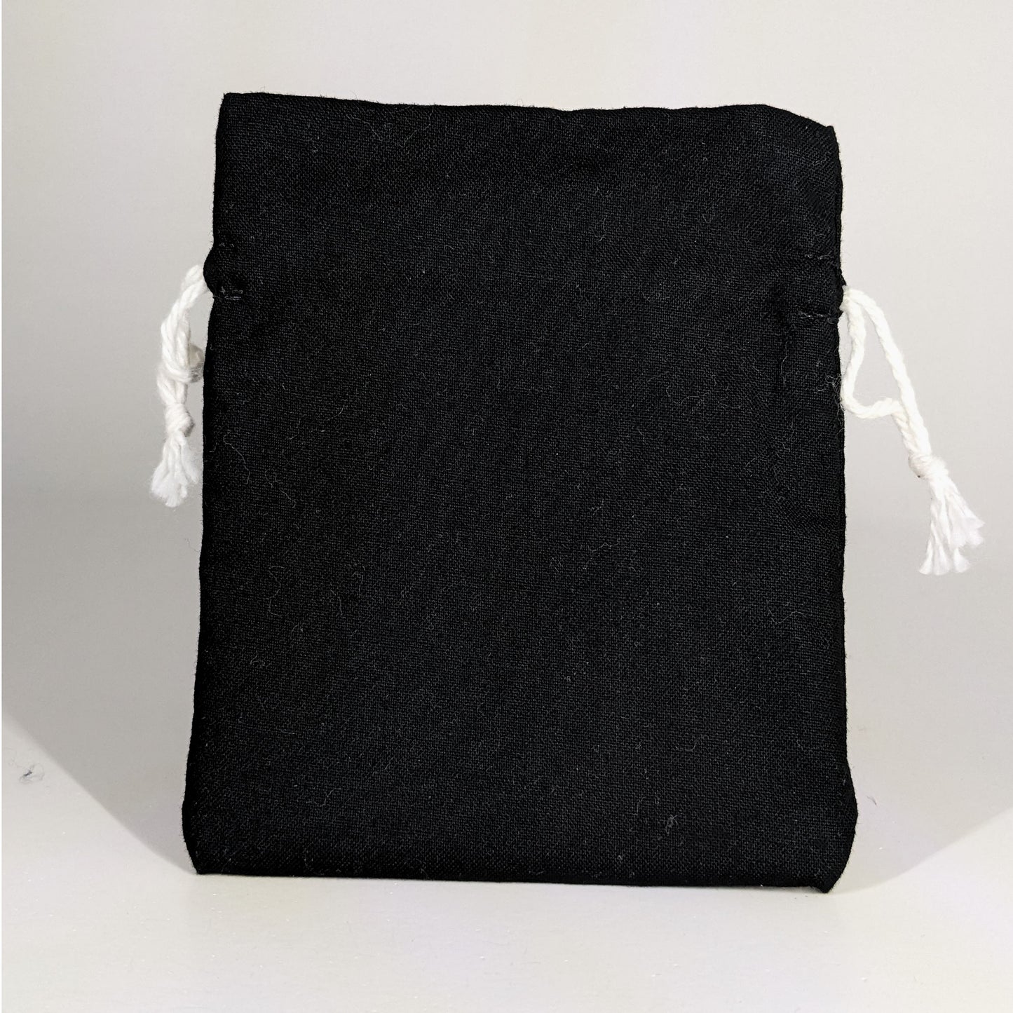 A small, handmade dice bag that is black stands upright on a white background.