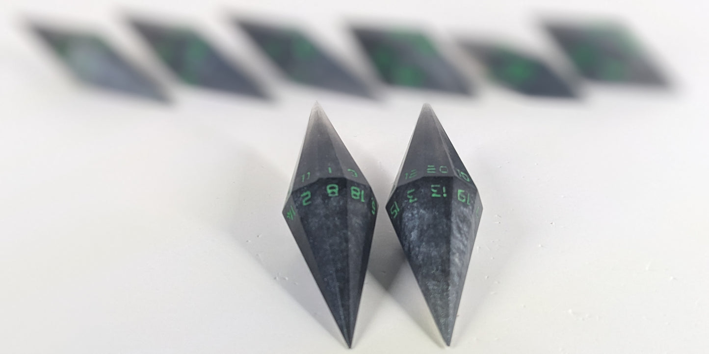 A stylized macro shot focusing heavily on 2 d20s from a shadowy swirls of black and silver with acidic green numbers handmade dice set in the foreground. The sharp diamond edges of these front resin dice are crisp, while the rest of the matching artisan dice collection forms a softly blurred background, creating depth.