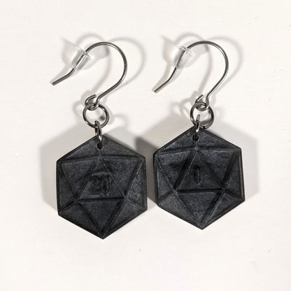 A pair of black and dark silver dangly, flat d20 earrings with silver color titanium and niobium hardware and bell shaped rubber backs on a white background. The earring on the left has a 20 on it and the earring on the right has a 1 on it, both in a fantasy style font.