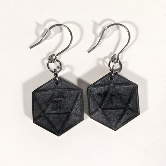 A pair of black and dark silver dangly, flat d20 earrings with silver color titanium and niobium hardware and bell shaped rubber backs on a white background. The earring on the left has a 20 on it and the earring on the right has a 1 on it, both in a fantasy style font.