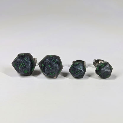 Two pairs of handmade d20 earrings that are black and silver with acid green numbers on a white background sit in a line with the larger pair on the left and the smaller pair on the right. The earrings on the left of each pair centers the 20 face and the earrings on the right of each pair centers the 1 face.
