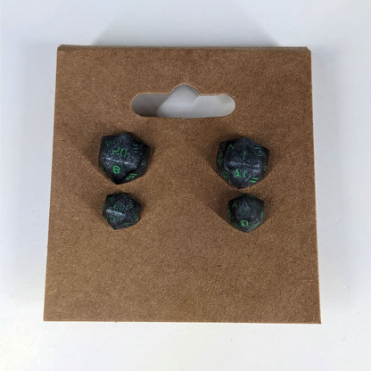 Two pairs of handmade d20 earrings that are black and silver with acid green numbers on a kraft brown earring card. The earrings on the left of each pair centers the 20 face and the earrings on the right of each pair centers the 1 face.