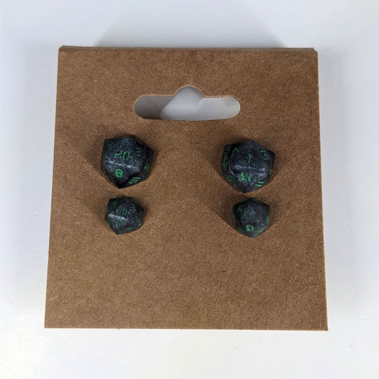 Two pairs of handmade d20 earrings that are black and silver with acid green numbers on a kraft brown earring card. The earrings on the left of each pair centers the 20 face and the earrings on the right of each pair centers the 1 face.