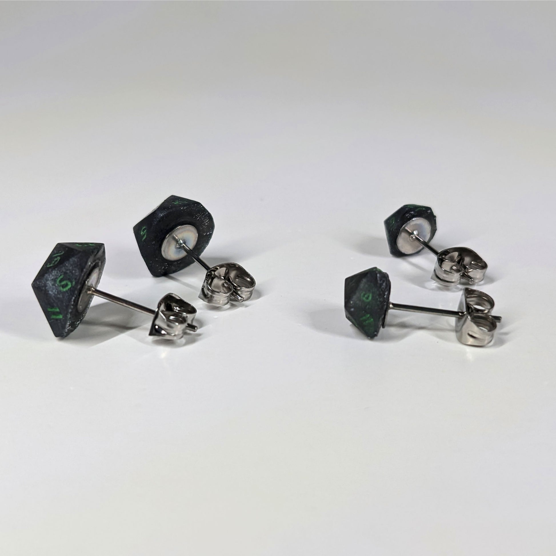 Two pairs of handmade d20 earrings that are black and silver with acid green numbers turned to show the metal alloy hardware and butterfly backs.