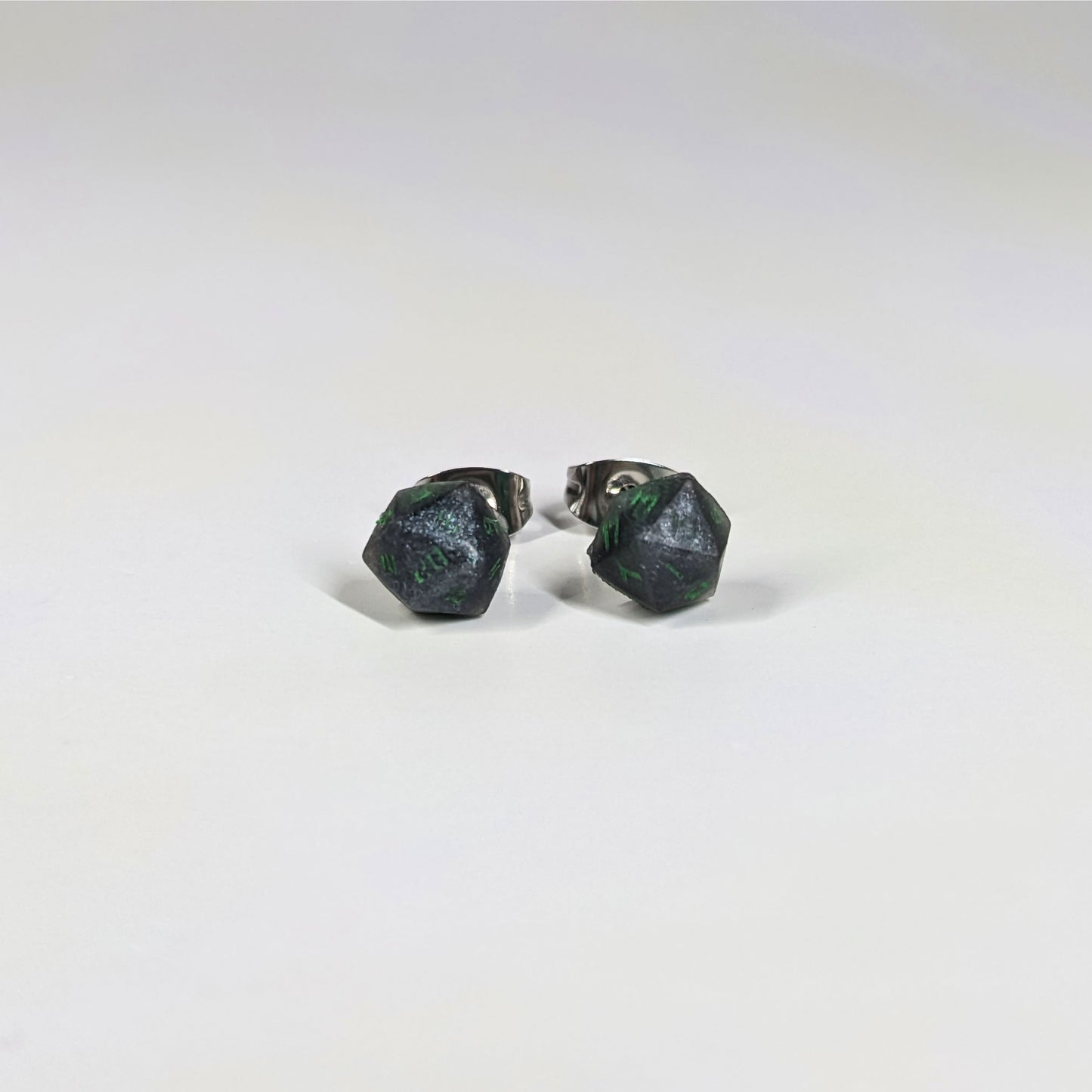 A single pair of the smaller size handmade d20 earrings that are black and silver with acid green numbers on a white background. The earring on the left centers the 20 face and the earring on the right centers the 1 face.