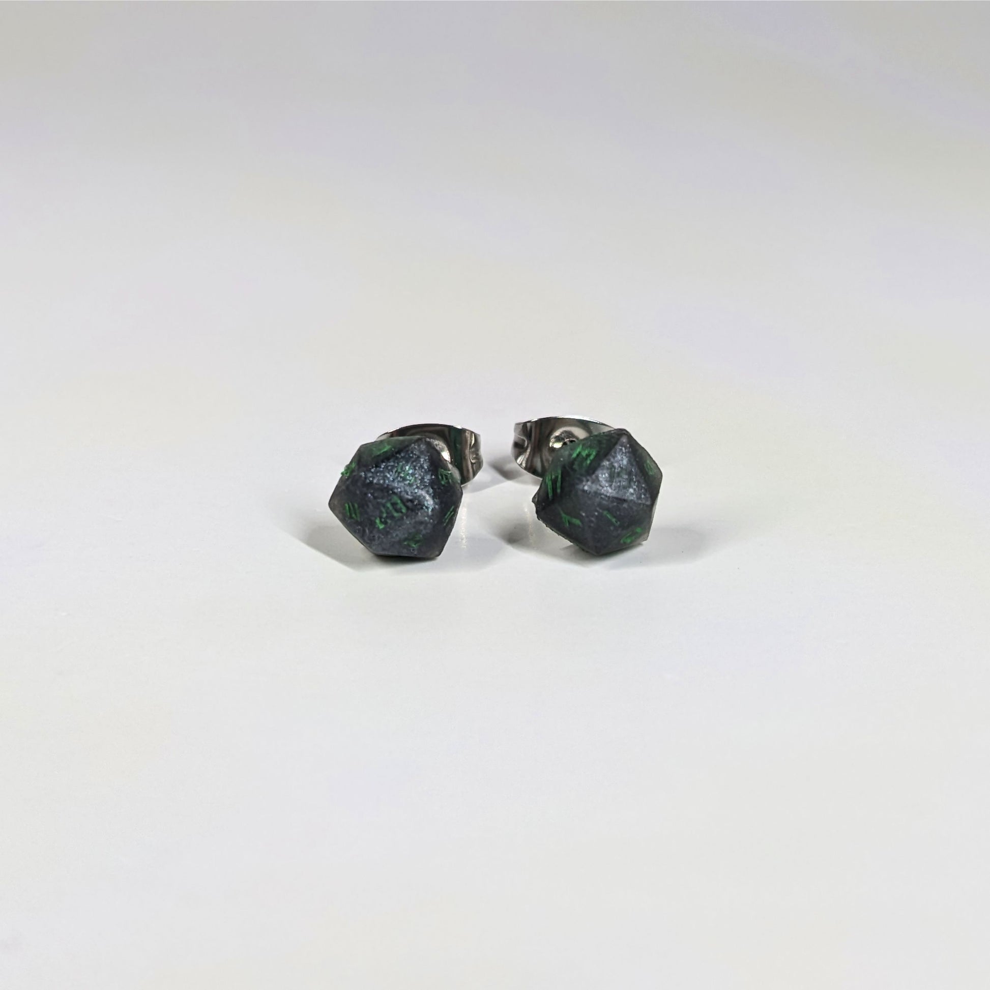 A single pair of the smaller size handmade d20 earrings that are black and silver with acid green numbers on a white background. The earring on the left centers the 20 face and the earring on the right centers the 1 face.