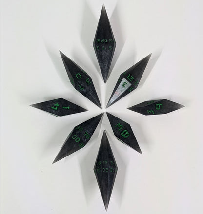 A complete set of diamond shaped resin dice featuring 2 d20s. These handmade dice shadowy swirls of black and silver with acidic green numbers and are clustered in a circle with the bottom points angled toward a central point on a white background.