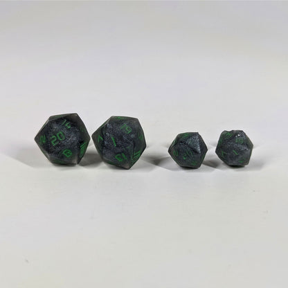Two pairs of handmade d20 earrings with sterling silver hardware that are black and silver with acid green numbers on a white background sit in a line with the larger pair on the left and the smaller pair on the right. The earrings on the left of each pair centers the 20 face and the earrings on the right of each pair centers the 1 face.