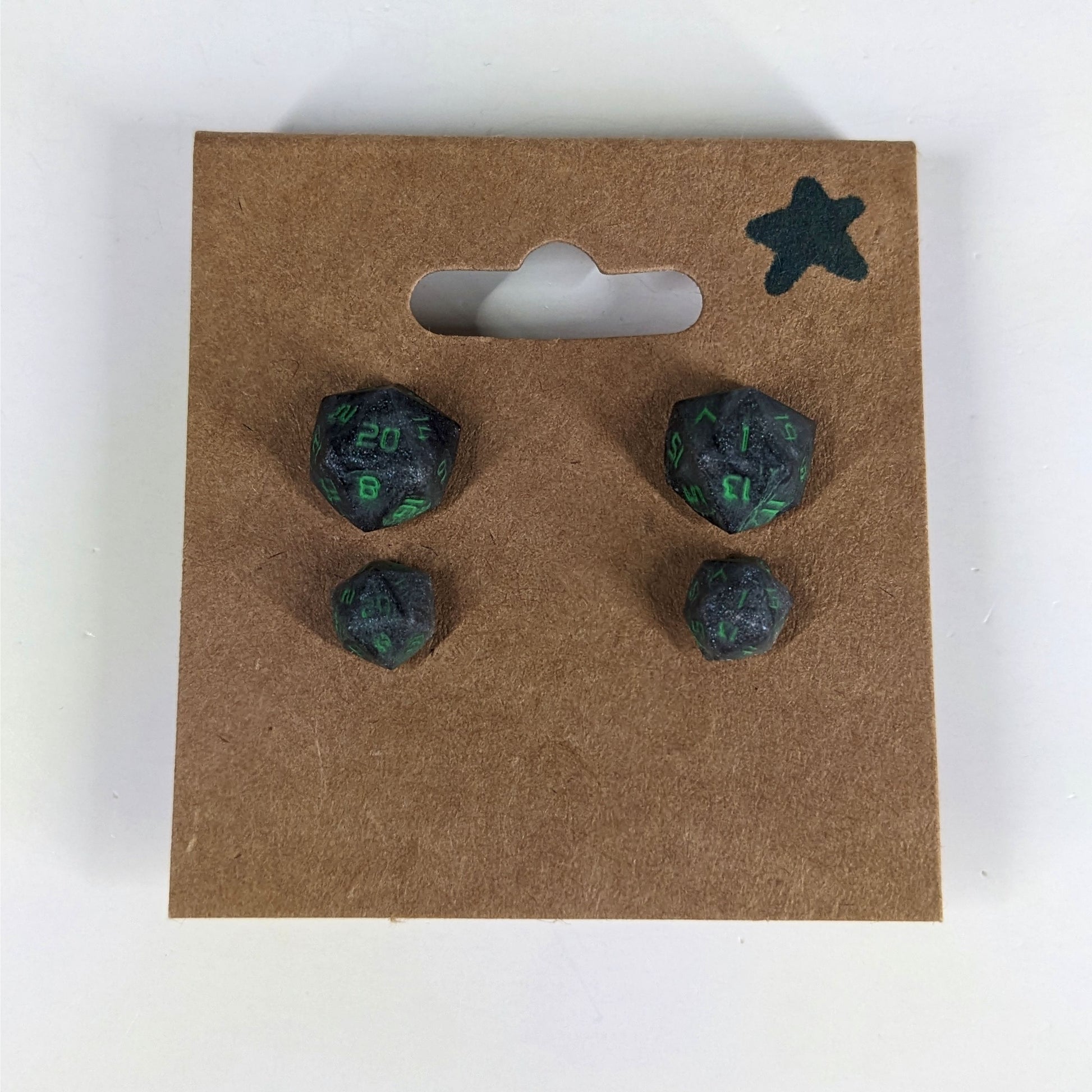 Two pairs of handmade d20 earrings with sterling silver hardware that are black and silver with acid green numbers on a kraft brown earring card with a star in the top right corner. The earrings on the left of each pair centers the 20 face and the earrings on the right of each pair centers the 1 face.
