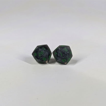 A single pair of the larger size handmade d20 earrings with sterling silver hardware that are black and silver with acid green numbers on a white background. The earring on the left centers the 20 face and the earring on the right centers the 1 face.