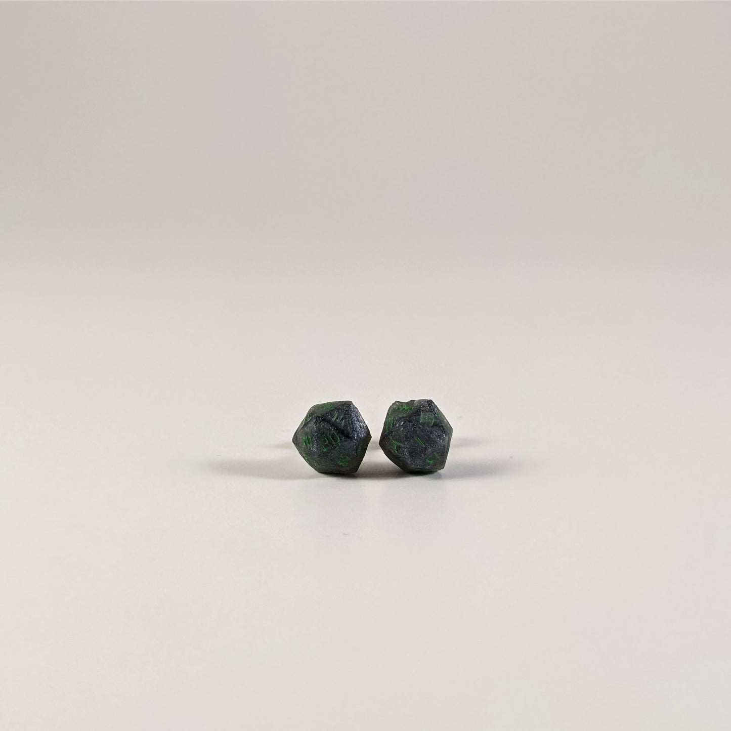 A single pair of the smaller size handmade d20 earrings with sterling silver hardware that are black and silver with acid green numbers on a white background. The earring on the left centers the 20 face and the earring on the right centers the 1 face.