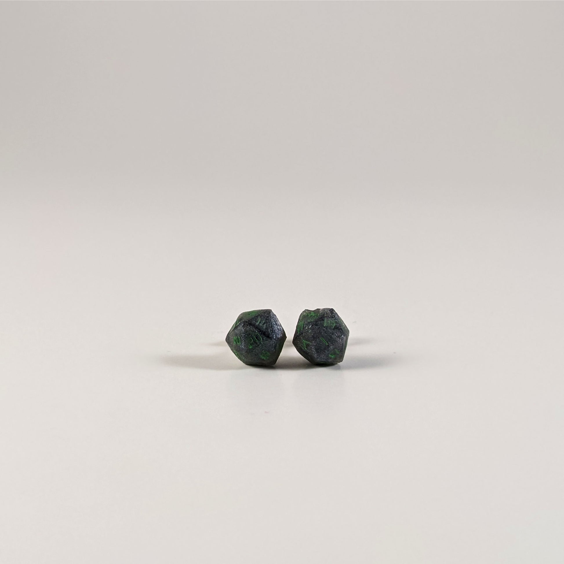 A single pair of the smaller size handmade d20 earrings with sterling silver hardware that are black and silver with acid green numbers on a white background. The earring on the left centers the 20 face and the earring on the right centers the 1 face.