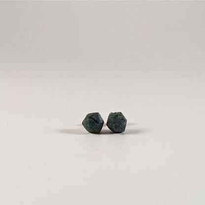 A single pair of the smaller size handmade d20 earrings with sterling silver hardware that are black and silver with acid green numbers on a white background. The earring on the left centers the 20 face and the earring on the right centers the 1 face.