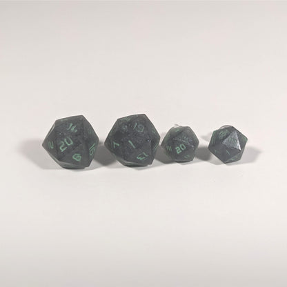 Two pairs of handmade d20 earrings with titanium hardware that are black with a touch of silver with acidic green numbers on a white background sit in a line with the larger pair on the left and the smaller pair on the right. The earrings on the left of each pair centers the 20 face and the earrings on the right of each pair centers the 1 face.