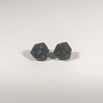 A single pair of the larger size handmade d20 earrings with titanium hardware that are black with a touch of silver with acidic green numbers on a white background. The earring on the left centers the 20 face and the earring on the right centers the 1 face.