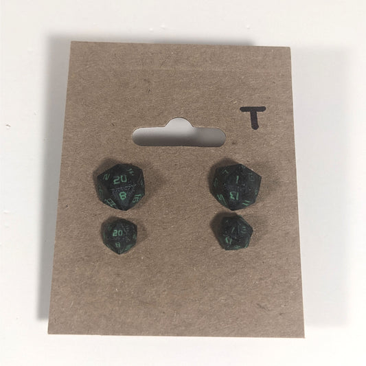 Two pairs of handmade d20 earrings with titanium hardware that are black with a touch of silver with acidic green numbers on a kraft brown earring card with a T in the top right corner. The earrings on the left of each pair centers the 20 face and the earrings on the right of each pair centers the 1 face.